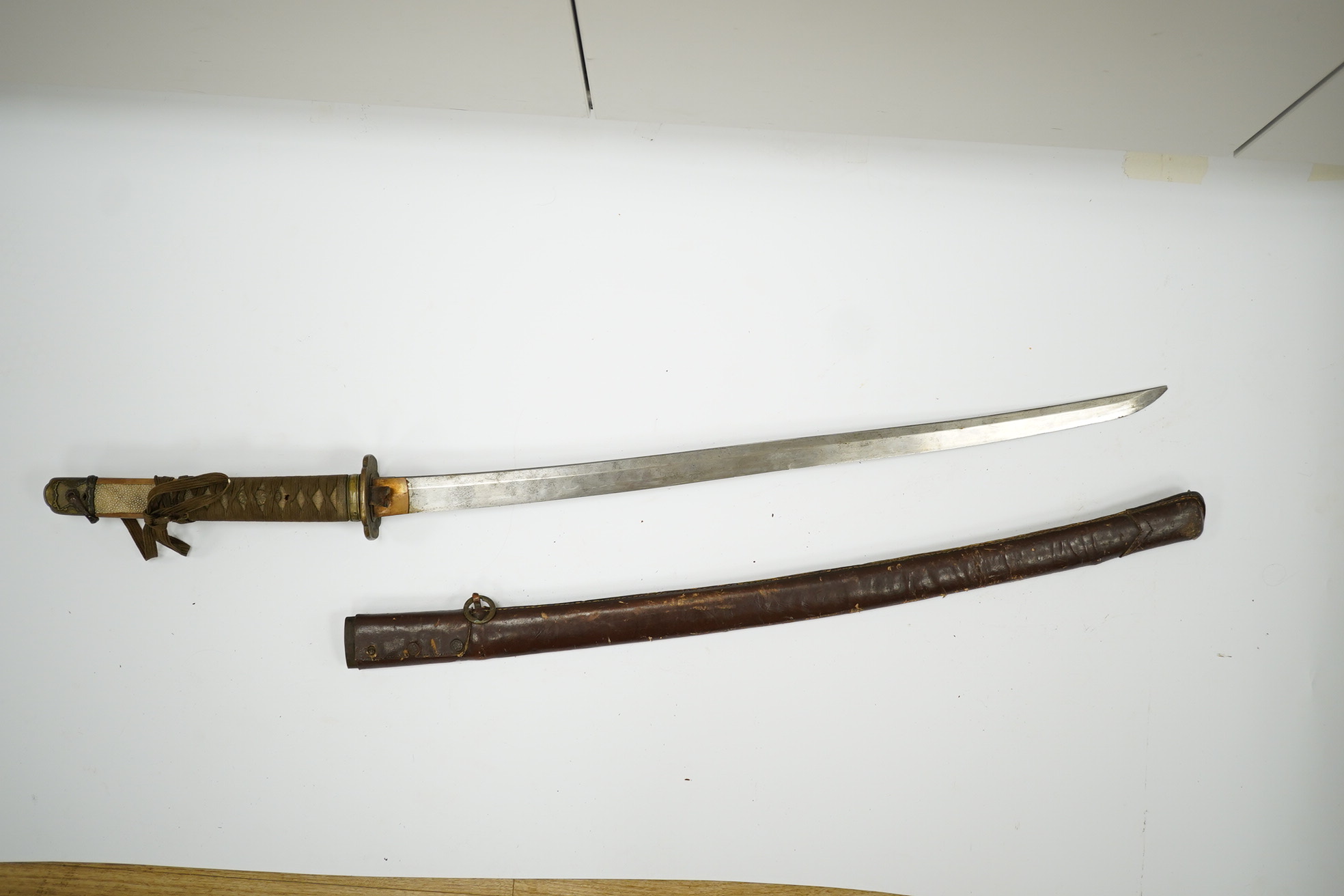 A WWII Japanese army officer’s Shingunto sword katana, blade 66.4cm, signed with Showa to stamp (tip of blade damaged), with unusual brass mounts, in its leather covered combat scabbard. Condition - poor to fair